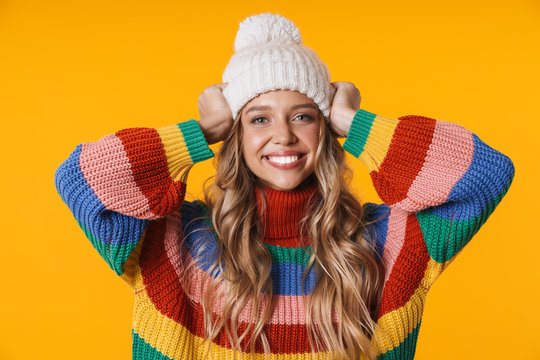 Image of cheerful young woman in winter hat and sweater smiling at camera