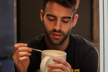 Happy young man drinking coffee with wooden spoon in a coffee shop