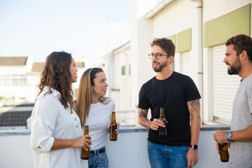 Obraz premium Group of old friends drinking beer and enjoying discussion on outdoor terrace. Young men and women in casual meeting outside. Gathering together concept