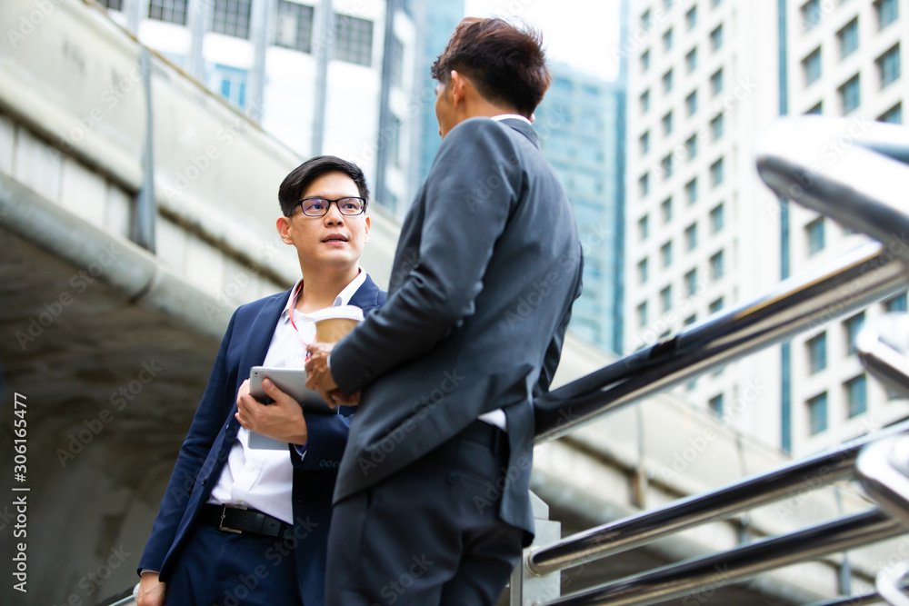 Wall mural image of two asian young businessmen walk and talk in the city