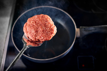 Burger patty on spatula on its way into the steaming hot frying pan