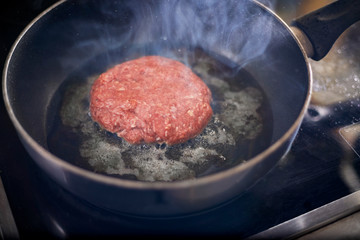 Burger patty amid oil being fried in the pan