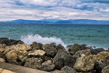 Seascape at stormy weather &ndash; waves at sea, large rocks on the shore, dark clouds on the sky and mountains on the horizon