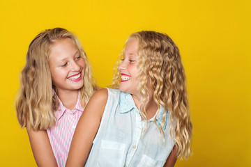 Happy sisters smiling and having fun together. Beauty and fashion. Cute twins girls on yellow background