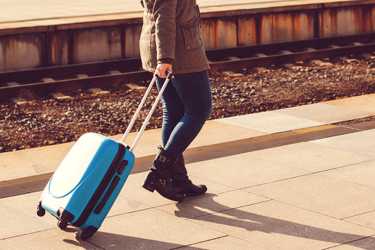 Girl dragging blue luggage suitcase. Travel concept. Woman at train station. Happy holiday vacation