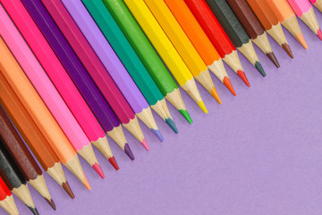 Close up row of colored pencils isolated against a purple background