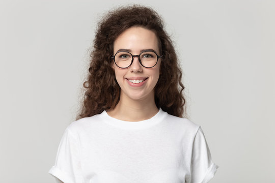 Smiling millennial girl in glasses posing on grey background