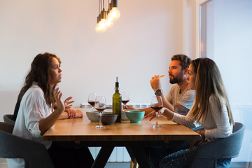 Group of friends drinking wine at dining table and chatting. Young men and women in casual meeting indoors. Friendly talk concept