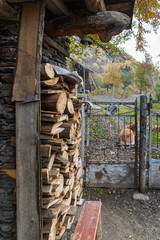 Fototapeta na wymiar A storehouse of firewood under a canopy near the metal gate of a house in Svaneti in the mountainous part of Georgia