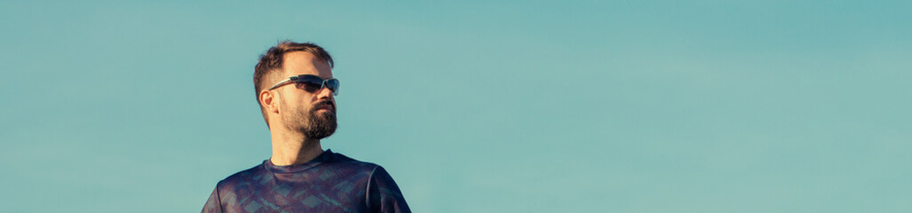 Athletic young guy with glasses looks into the distance. Toned panoramic image.