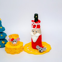 Home decor concept for new year and christmas. Photo of knitted decor thread for a bottle of champagne and a glass with a toy toy mouse, Christmas tree and yellow napkins on a white background.