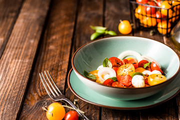 Yellow and red cherry tomatoes salad with fresh basil, mozzarella cheese and onion