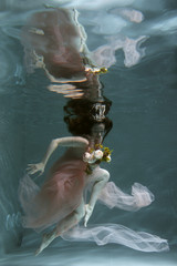 A girl with long dark hair swims underwater in a pink dress and with a crown on her head, like an underwater queen. Fairy tale suitable for advertising