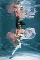 A girl with long dark hair swims underwater in a pink dress and with a crown on her head, like an underwater queen. Fairy tale suitable for advertising