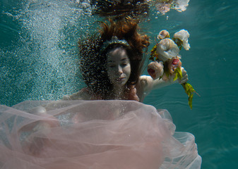 A girl with long dark hair swims underwater in a pink dress and with a crown on her head, like an underwater queen. Fairy tale suitable for advertising