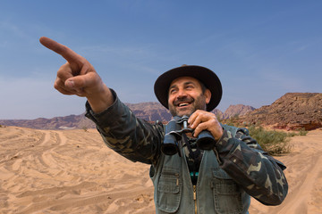 A hunter in a hat with binoculars looks out for prey	