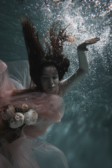 A girl with long dark hair swims underwater in a pink dress and with a crown on her head, like an underwater queen. Fairy tale suitable for advertising