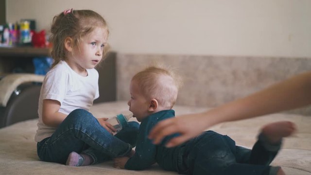 funny girl sucks teat on water bottle and gives to cute little baby brother but mother takes away in spacious room