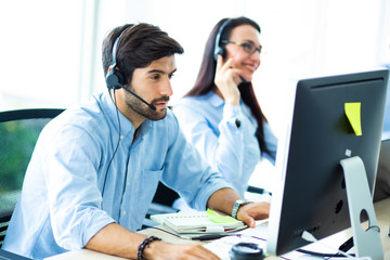 Attractive hansome business man in headsets while working with computer in customer service office