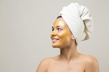 Beauty portrait of woman in white towel on head with gold nourishing mask on face. Skincare cleansing eco organic cosmetic spa relax concept.