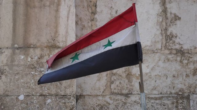A Syrian flag with wooden stick waving, wall background.