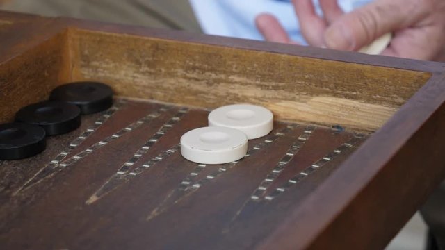 Slow motion close up shot, black and white chips inside the board of backgammon game, rolling a dice and picking it up.