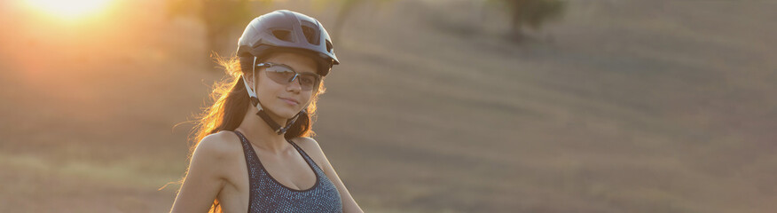 Girl on a mountain bike on offroad, beautiful portrait of a cyclist at sunset, Fitness girl rides a modern carbon fiber mountain bike in sportswear. Close-up portrait of a girl in a helmet and glasses