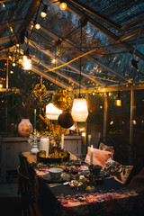 Decorated greenhouse in trendy christmas setting with dinner table, candles and christmas lights.