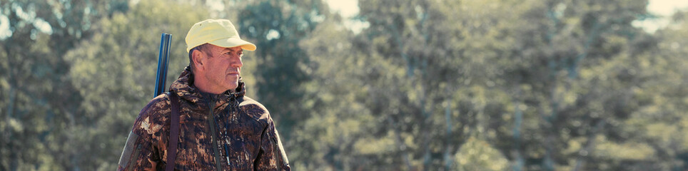 Hunter with a hat and a gun in search of prey in the steppe, Aims for prey. Panoramic image for your text, toned.