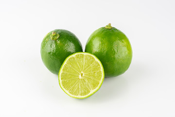 Group of green lemons with sliced lemon over white background.