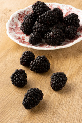 Blackberries on a decorated dish with blackberries over a wooden table.