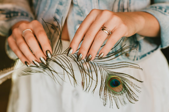 Stylish trendy female mirror manicure, metal nail art, holding peacock feather