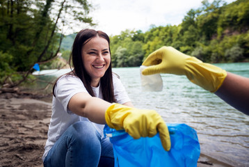 Smiling female volunteer cleaning garbage near river shore