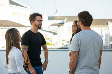 Happy friends drinking beer and sharing news on outdoor terrace. Young men and women in casual meeting outside. Friendly communication concept