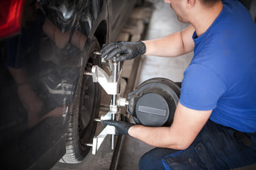 Wheel alignment. Car mechanic installing sensor during suspension adjustment
