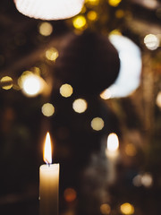 Macro close-up of a burning candle in christmas setting with blurry lights.