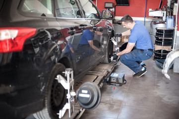 Fototapeta premium Wheel alignment. Car mechanic installing sensor during suspension adjustment