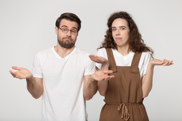 Confused millennial couple shrug shoulders feel baffled