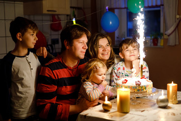 Obraz na płótnie Canvas Adorable little toddler girl celebrating second birthday. Baby child, two kids boys brothers, mother and father together with cake and candles. Happy healthy family portrait with three children