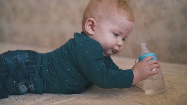 funny girl hugs little brother nibbling rubber teat of water bottle on large bed in spacious room extreme close view