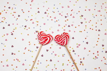 Two heart shape sweet lollipop on abstract background with little colorful candy’s. Valentine,  Christmas and New Year holiday concept decoration. Top view. 