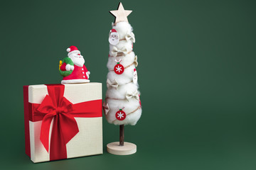 Gypsum colorful santa claus on the gift box and christmas tree with decorations over green background. Copy space