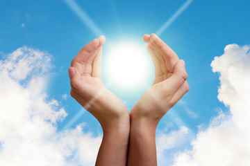 Hands hold the sun in palms on a background of blue sky with clouds. The concept of conservation of natural resources, the ozone layer. The concept of health, peace, wealth, prosperity, good luck