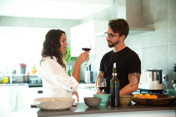 Happy millennial couple celebrating anniversary and drinking wine together in kitchen. Young man and woman in casual meeting indoors. Love and relationship concept