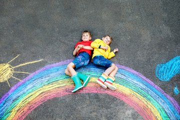two school kids boys having fun with with rainbow picture drawing with colorful chalks on asphalt....
