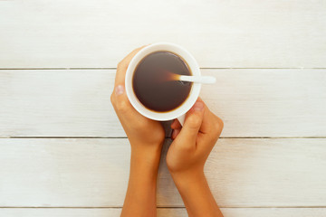 Children's hands holding a white mug with tea on a white wooden table background. Place for text. Blank for design, cards, congratulations. New Year and Christmas theme