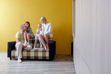 Big loving family mom dad sister and brother are sitting on sofa in living room on a yellow background. Concept of love happiness and positive in the family. Place for text