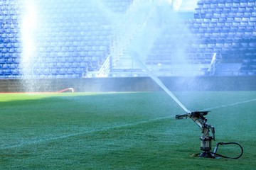 Watering green grass in stadium, Restoring field in morning after football match.