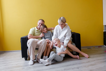 Big loving family mom dad sister and brother are sitting on sofa in living room on a yellow background. Concept of love happiness and positive in the family. Place for text