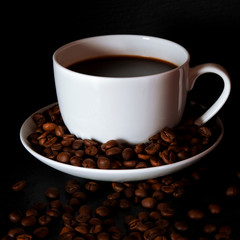A white cup with black fragrant coffee stands on a black background with coffee zurnes next to colorful french cookies macaroons